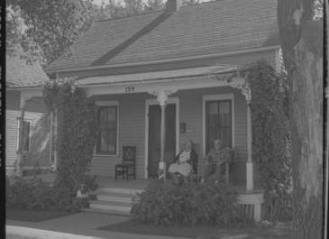 Fargo 1955 - Mr. and Mrs. Chris Eide sitting on front porch of house, 124 1st Avenue S, Fargo Cal Olson Photographer 