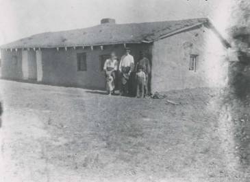 Ashley1916 - McIntosh County Photograph Collection - A family of six stands outside of a house of mud brick and sod construction near Ashley. Mrs. T.C. Thorn. 